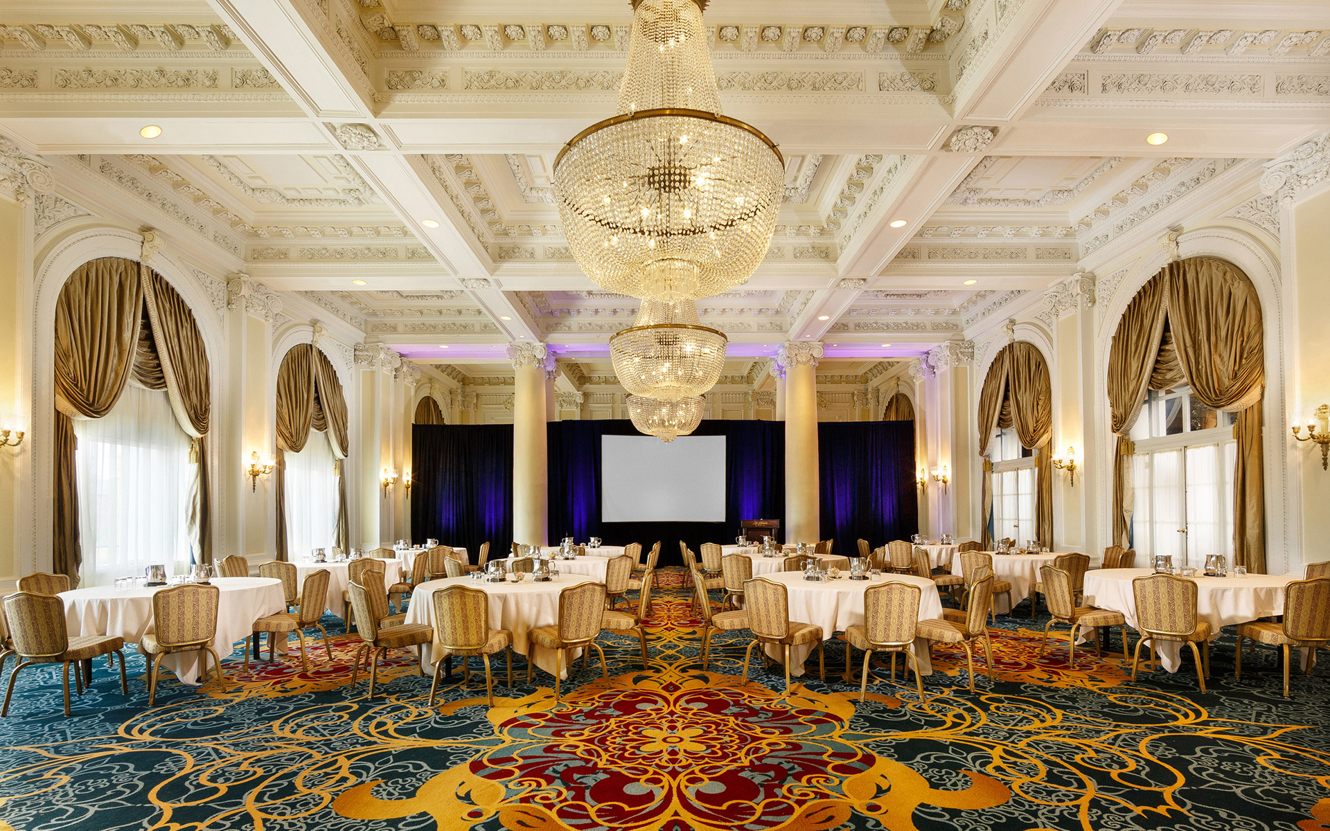 A large, ornate meeting room with a projector screen, tables, and chairs.